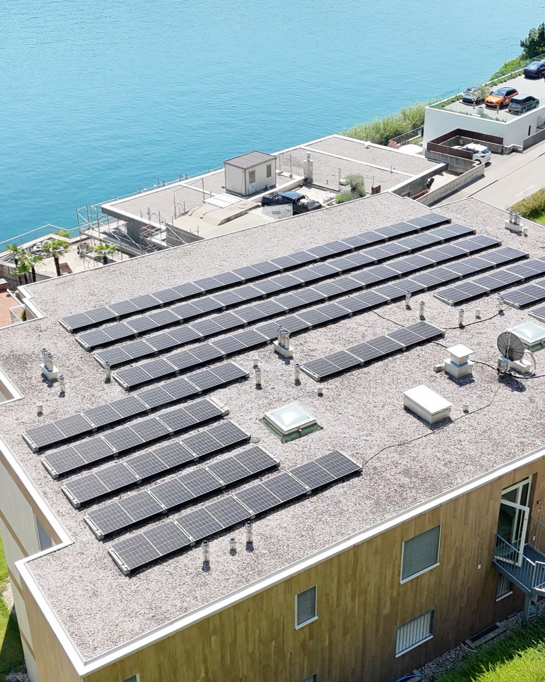 Veduta aerea di un edificio residenziale affacciato sul lago, con le file di moduli fotovoltaici installate sul tetto piano.